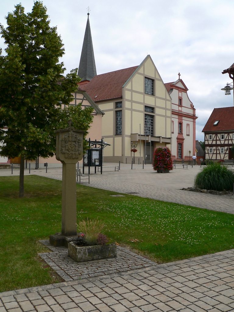 Die beiden Giebel der Pfarrkirche St. Johannes der Täufer säumen in Stadtlauringen die obere Seite des Marktplatzes, die des Rathauses die untere. 