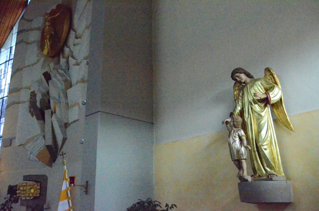 Das Stuckrelief von Hubert Elsässer wurde erst 1984 als Altarbild in der 17 Jahre zuvor eingeweihten Neuen Schutzengelkirche eingebaut. Die namensgebende Schutzengelstatue stammt aus der früheren Pfarrkirche.