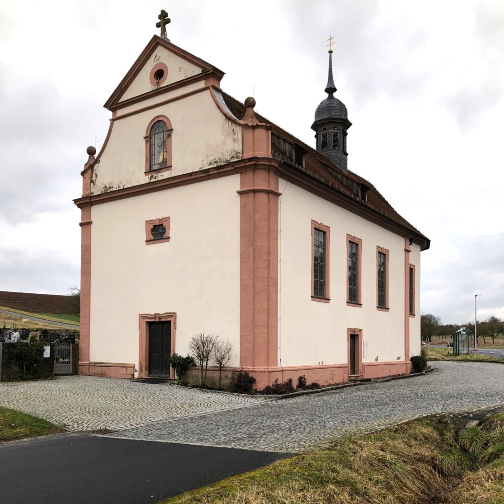 Bekannter als die Pfarrkirche St. Jakobus ist diese dem heiligen Kreuz geweihte Kapelle, zumal sie unmittelbar an der B 287 nahe der Autobahnanschlussstelle Hammelburg steht.