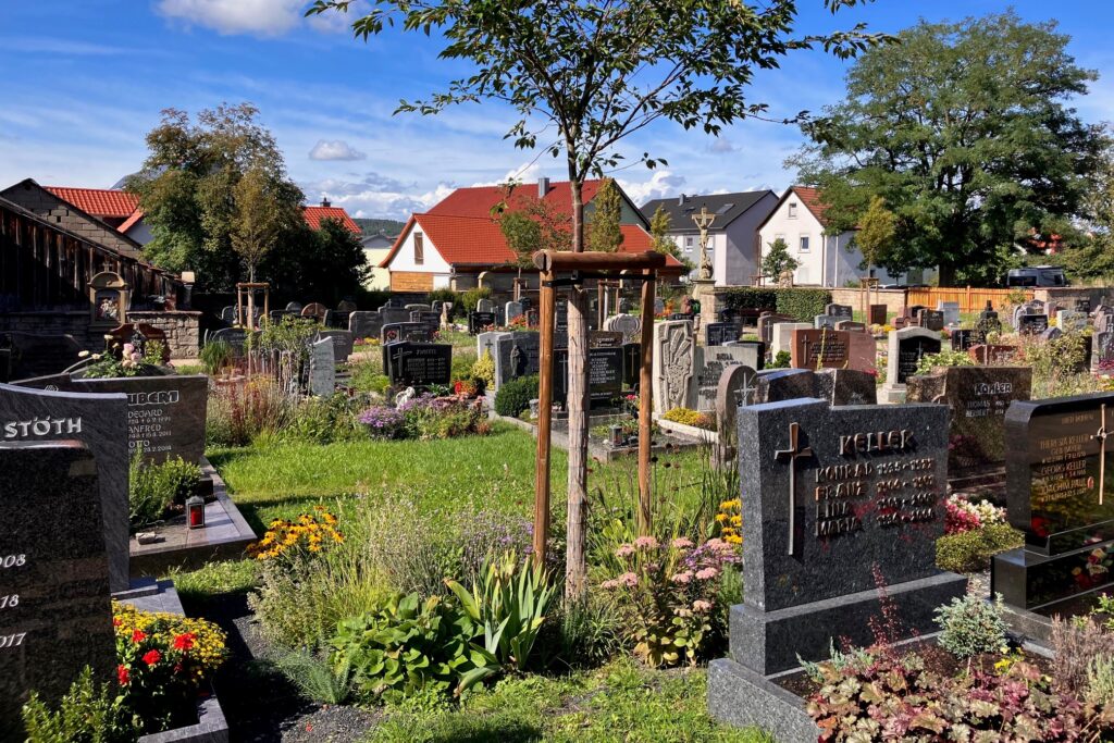 Ein Friedhof mit Gräbern in akkurater geometrischer Ausrichtung. An den Stirnseiten der großzügig bemessenen Ruheplätze für die Verstorbenen stehen meist schwarze, breite Grabsteine mit dem Namen sowie dem Geburts- und Sterbedatum der betreffenden Personen.