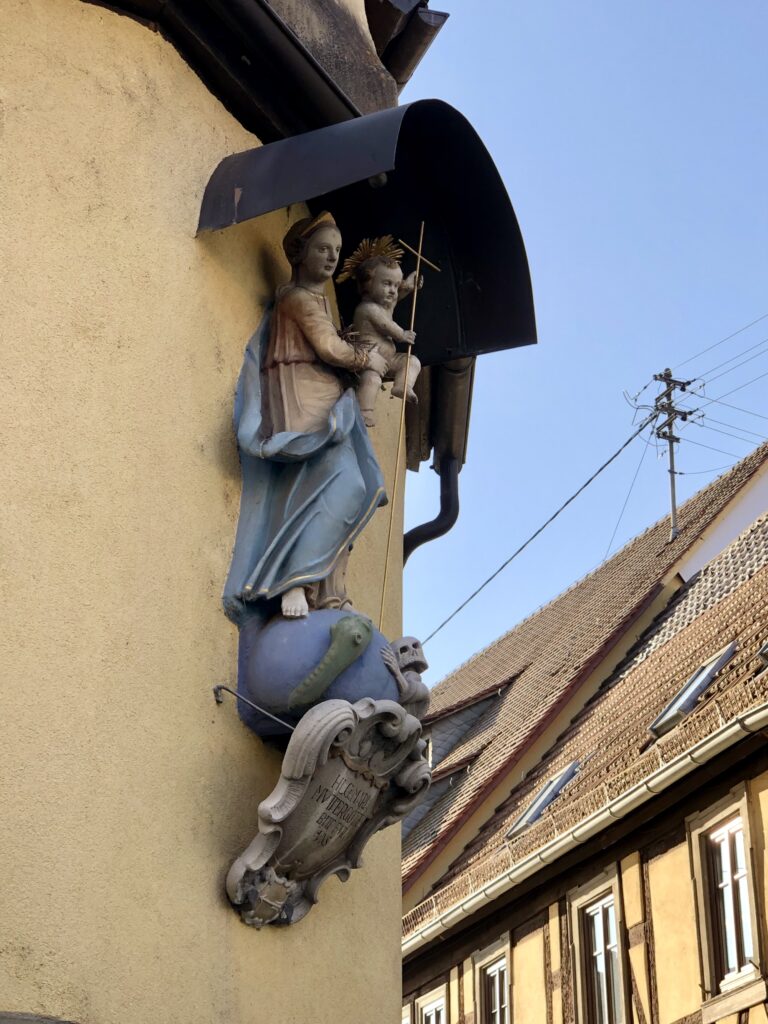 Die Gottesmutter (Hausmadonna) zertritt das Böse (Schlange) auf der Erdkugel.